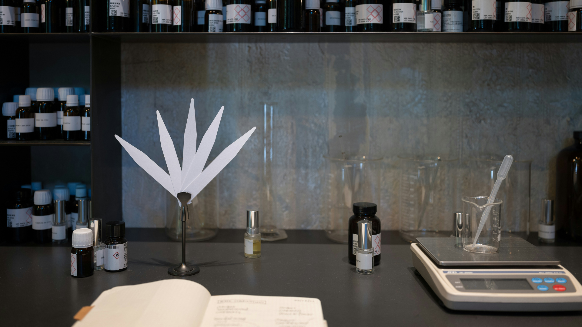 A perfumer's workbench with fragrance materials, a balance, glassware, blotters and a formulation notebook